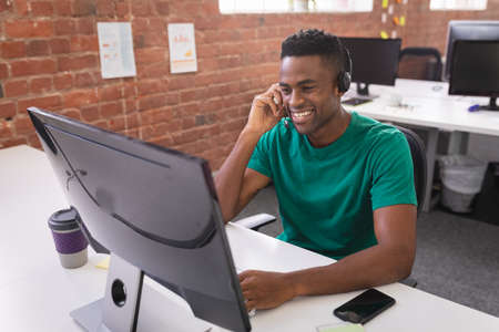 African american businessman having video call sitting in front of computer using headphones....