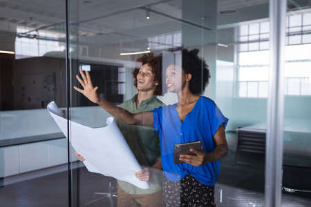 Diverse male and female colleagues in office discussing over blueprint document. independent...