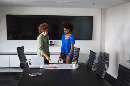 Diverse male and female colleagues in office discussing over blueprint document. independent...