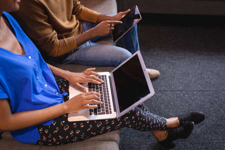 Diverse male and female colleagues working sititng on sofa in office using computer and tablet. independent creative design business.の写真素材