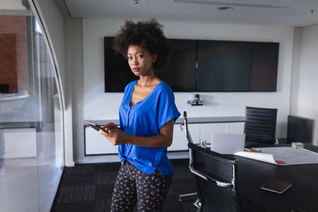 African american business woman in meeting room standing over blueprint document. independent...