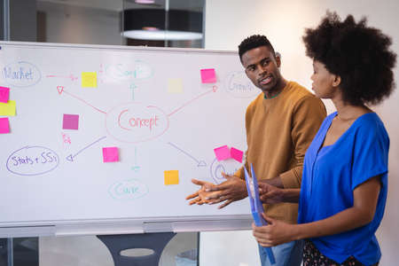Diverse male and female colleagues standing in front of whiteboard having discussion. independent...