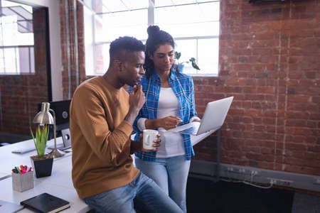 Diverse male and female colleagues at work standing discussing in front of laptop. independent...