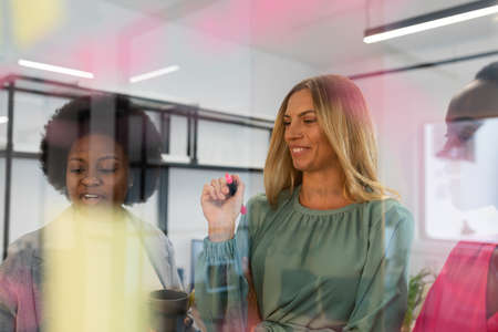 Diverse group of business colleagues brainstorming in meeting room using glass wall. business in a...