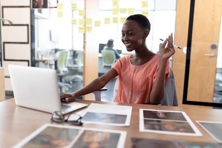 Happy african american businesswoman sitting at desk having video call conversation using laptop....