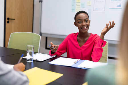 African american businesswoman in discussion at work smiling to business colleagues. working person in a modern officeの写真素材