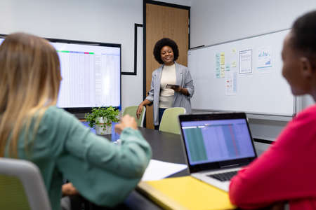 African american businesswoman giving presentation to diverse group of colleagues in meeting room....