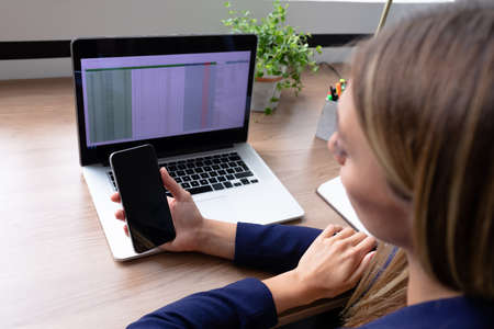 Caucasian businesswoman sitting at desk having video call conversation using smartphone. business in...