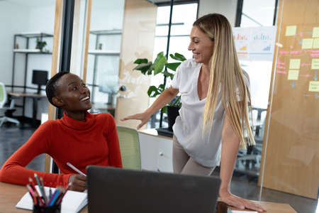 Diverse female business colleagues in discussion at work smiling in meeting room. business in a modern office.の写真素材