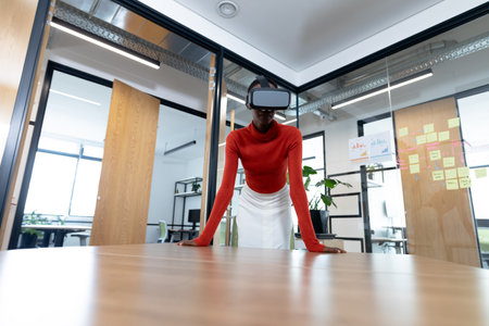 African american businesswoman leaning on desk and using vr headset in meeting room. business in a...