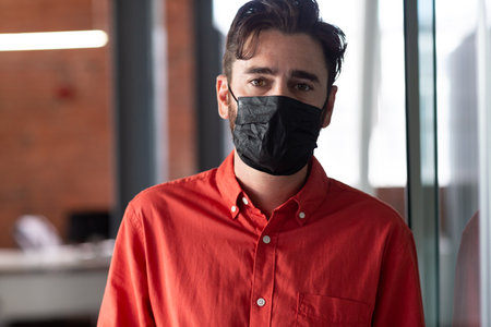 Portrait of caucasian businessman wearing face mask standing in corridor. independent creative...