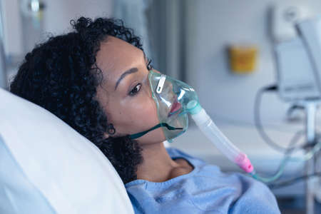 Worried african american female patient in hospital bed with oxygen ventilator. medicine, health and healthcare services during coronavirus covid 19 pandemic.の写真素材