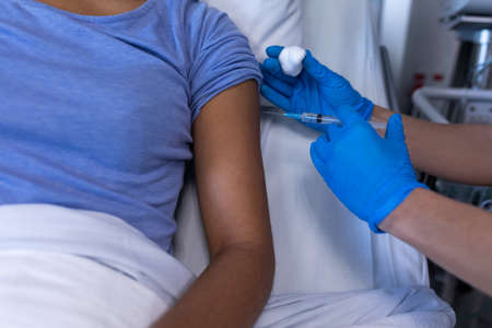 Midsection of caucasian female doctor in hospital vaccinating african american female patient....
