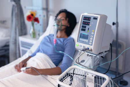 Ventilator monitor and african american female patient in hospital bed with oxygen ventilator. medicine, health and healthcare services during coronavirus covid 19 pandemic.の写真素材