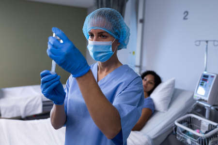 Caucasian female doctor wearing face mask preparing vaccination for african american female patient. medical professional at work during coronavirus covid 19 pandemic.の写真素材