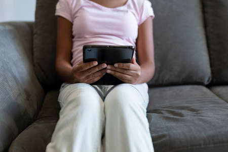 Midsection of mixed race girl sitting on couch using digital tablet. teenage lifestyle, leisure time, communication and technology.の写真素材