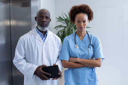 Portrait of diverse male and female doctors holding tablet in hospital corridor. medical professional at work.の写真素材