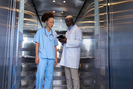 Serious diverse female and male doctors using tablet in hospital lift. medical professionals at work.の写真素材