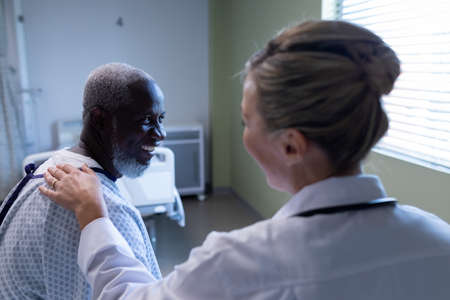 Diverse female doctor and male patient sitting on hospital bed smiling to each other. medicine, health and healthcare services.の写真素材