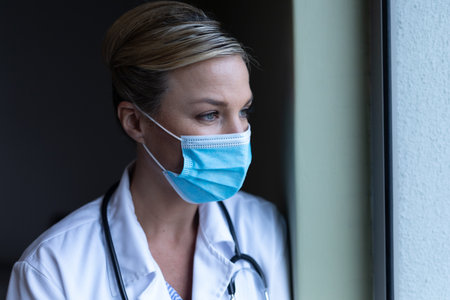 Portrait of caucasian female doctor wearing mask looking ahead. medicine, health and healthcare services during coronavirus covid 19 pandemic.の写真素材