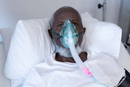 African american male patient lying on hospital bed wearing oxygen mask ventilator. medicine, health and healthcare services during coronavirus covid 19 pandemic.の写真素材