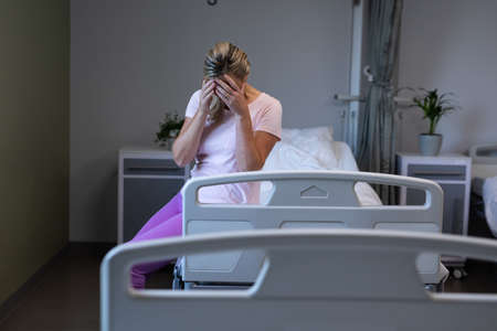 Caucasian female patient sitting on hospital bed in patient room worrying. medicine, health and...