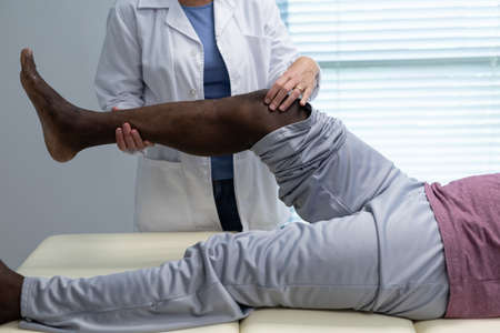 Midsection of caucasian female physiotherapist bending knee of african american male patient....
