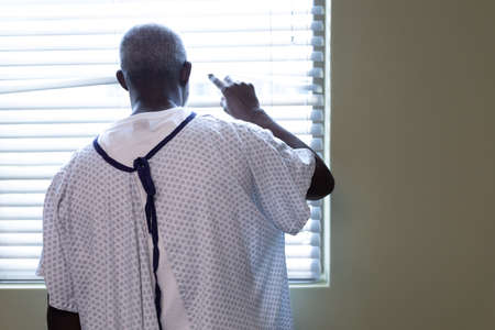 Portrait of african american male patient looking through the window in hospital patient room....