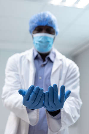 Portrait of african american male doctor wearing face mask surgical cap and latex gloves. medicine, health and healthcare services during coronavirus covid 19 pandemic.の写真素材