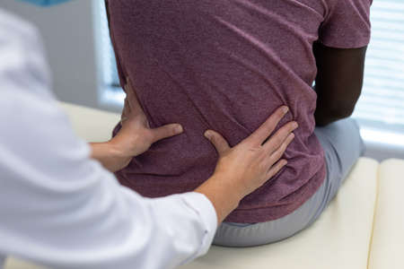 Midsection of caucasian female physiotherapist palpating back of african american male patient. medicine, health and healthcare servicesの写真素材