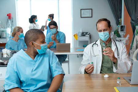 Caucasian male doctor in face mask preparing covid vaccination for female colleague in hospital....