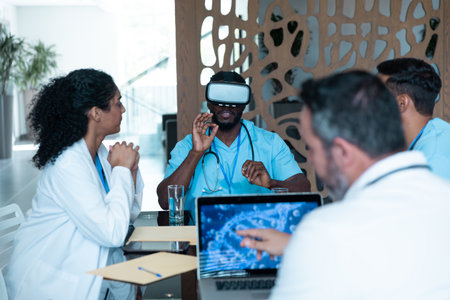Diverse male and female doctors wearing face masks sitting at table and using vr glasses. medicine, health and healthcare services.の写真素材