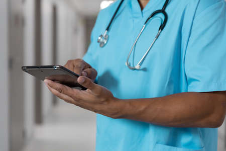Midsection of mixes race male doctor standing in corridor using tablet. medicine, health and...