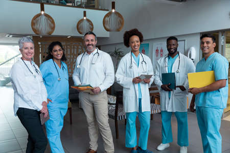 Portrait of group of diverse male and female doctors standing in hospital corridor smiling to...