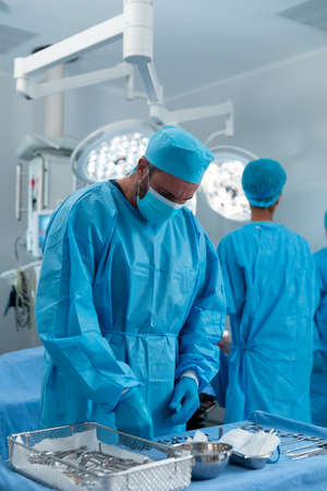 Caucasian male surgeon wearing face mask and protective clothing in operating theatre. medicine,...