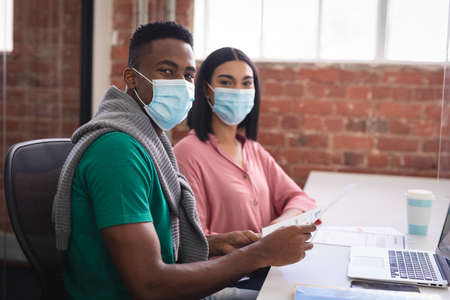 Portrait of diverse creative colleagues wearing face masks brainstorming in meeting room....