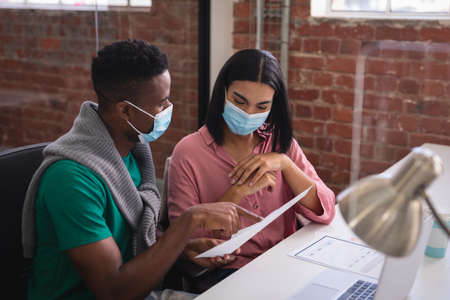 Diverse creative colleagues wearing face masks brainstorming in meeting room. independent creative design business during covid 19 coronavirus pandemic.の写真素材