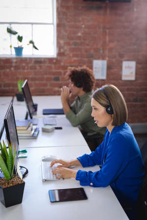 Asian businesswoman sitting in front of computer wearing headset having video call. independent...
