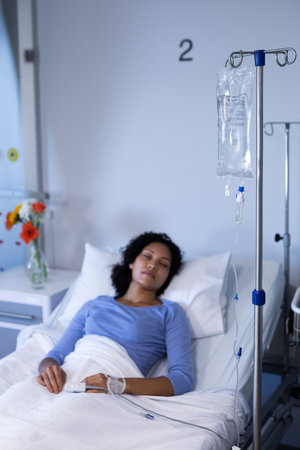 Mixed race female patient lying asleep in hospital bed wearing fingertip pulse oximeter and iv drip....
