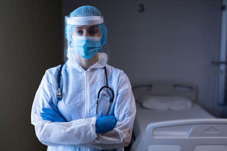 Caucasian female doctor in hospital wearing ppe suit, face mask, face shield and medical cap. medical professional at work and protective clothing during coronavirus covid 19 pandemic.の写真素材