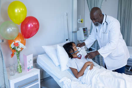 African american male doctor putting oxygen mask ventilator on sick mixed race girl in hospital bed....