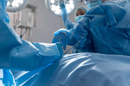 Diverse group of male and female surgeons in operating theatre wearing face masks performing...