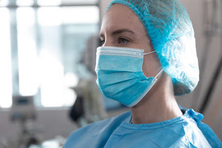 Portrait of caucasian female surgeon standing in operating theatre wearing face mask. medicine, health and healthcare services during coronavirus covid 19 pandemic.の写真素材