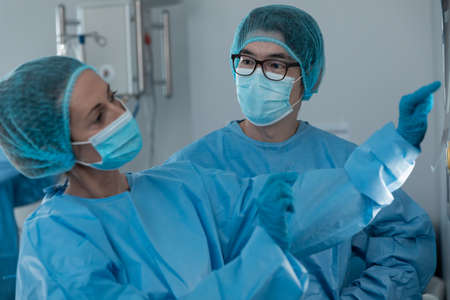 Diverse couple of male and female surgeons in operating theatre wearing face masks looking at screen. medicine, health and healthcare services during coronavirus covid 19 pandemic.の写真素材