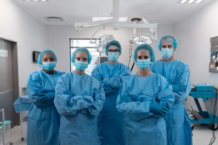 Diverse group of male and female surgeons standing in operating theatre wearing protective overalls. medicine, health and healthcare services during coronavirus covid 19 pandemic.の写真素材