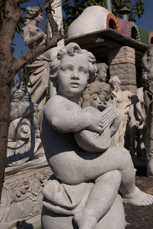 Ancient stone sculpture of naked cherub playing lute in reclamation yard. art and classical style romantic figurative stone sculpture.の写真素材