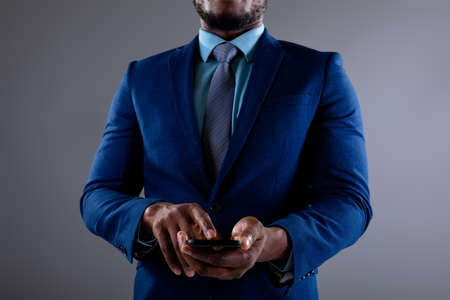 Mid section of african american businessman using smartphone against grey background. business, professionalism and technology conceptの写真素材
