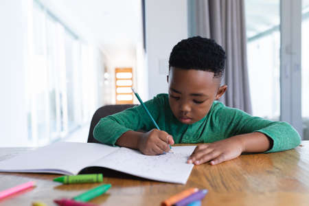 African american boy in online school class, writing in his notebook. at home in isolation during...