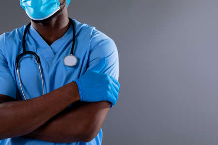 Mid section of african american male health worker wearing face mask against grey background. healthcare and medical professionalism conceptの写真素材