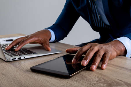 Close up of businessman using laptop and digital tablet against grey background. business, professionalism and technology conceptの写真素材